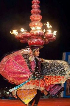 a woman is dancing with fire in her hand and holding an umbrella on her head