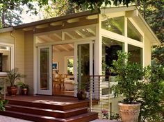 a small house with sliding doors on the front and side windows in the back, surrounded by greenery