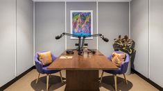 a desk with two chairs and a painting on the wall in an office space that is well lit