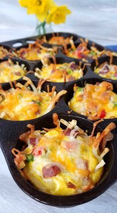 a muffin tin filled with breakfast food on top of a table next to a yellow flower