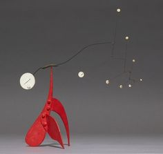 a red sculpture with white balls hanging from it's sides and an object in the air