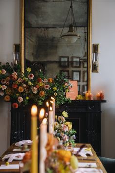 a dining room table with flowers and candles on it, in front of a mirror