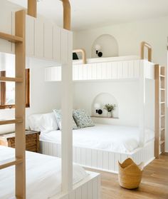 a bedroom with bunk beds and white walls, wood flooring and wooden ladders