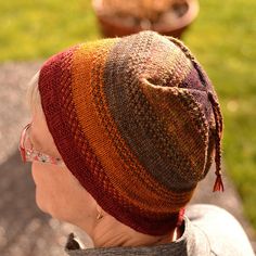 a woman wearing a knitted hat sitting on top of a wooden bench in the grass