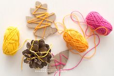 three balls of yarn and two pine cones on a white surface with twine