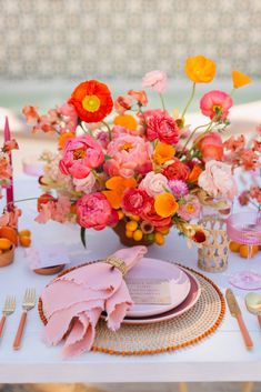 the table is set with pink and orange flowers in vases, plates, utensils and napkins