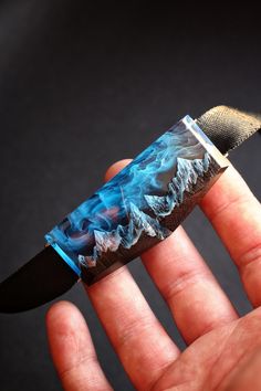 a hand holding a blue and black knife in it's left hand with flames coming out of the blade