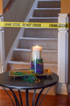 a candle and beads sit on a table in front of a staircase with caution tape