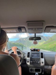 two people in the back seat of a car driving down a road with mountains in the background