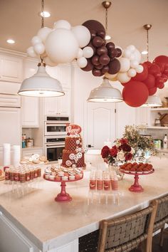 balloons are hanging from the ceiling above a kitchen counter with desserts and drinks on it