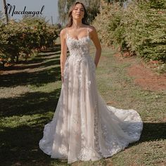 a woman standing in an apple orchard wearing a wedding dress with spaghetti straps and open back