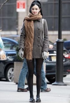 a woman walking down the street with a scarf around her neck and gloves on,