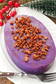 a purple cake on a white plate next to a fork and holly tree with red berries