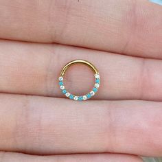 a person's hand holding a gold ring with turquoise stones on it and a diamond set in the middle