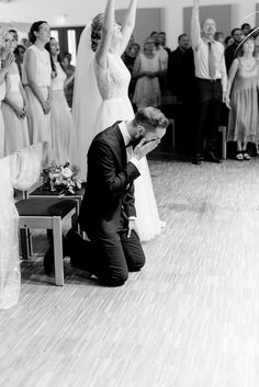 a man kneeling down next to a woman in front of a group of other people