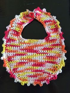 a crocheted bib hanging on a black background with white, red, yellow and pink stripes