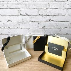 two open boxes with black and gold trims on them sitting on a table next to a white brick wall