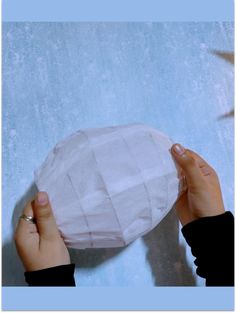 two hands holding up a paper ball on a blue background with birds in the sky