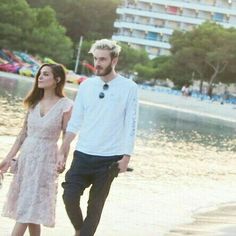 a man and woman walking on the beach holding hands