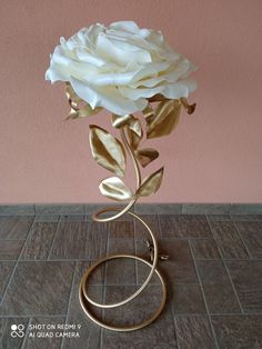 a white rose on a gold stand against a pink wall