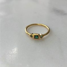 a gold ring with two green stones on the front and one yellow stone on the back