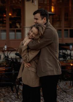 a man and woman embracing each other in front of a building with tables on it