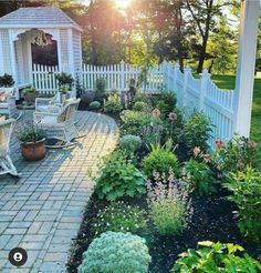 a garden with flowers and plants in the middle of it, next to a white picket fence