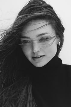 a black and white photo of a woman with her hair blowing in the wind, looking at the camera