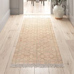 a white vase sitting on top of a wooden floor next to a rug in front of a doorway