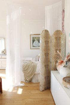 a bedroom with white walls and wooden flooring, two tall decorative objects in the foreground