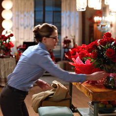 a woman reaching out to touch a vase filled with red flowers