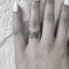 a woman's hand with a butterfly tattoo on it and the other hand has white nails