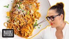 a woman with glasses is looking at a plate of pasta on the table in front of her