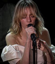 a woman holding a microphone in her right hand and singing into the microphone with both hands