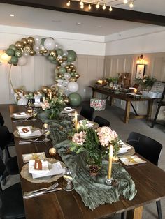 a table set for a party with balloons and greenery on the wall behind it