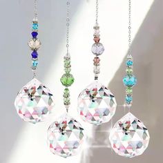 four crystal ornaments hanging from chains in the shape of balls and diamonds, all with different colored stones