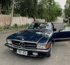 a blue mercedes benz is parked on the street in front of a fenced area