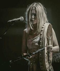 a woman with long blonde hair holding a musical instrument in front of a microphone on stage