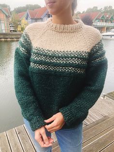 a woman standing on a dock wearing a green and white sweater