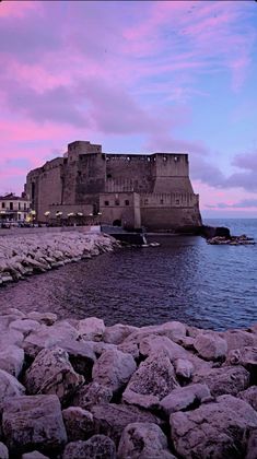 an old castle sitting on top of a rocky shore next to the ocean at dusk