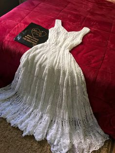 a white dress laying on top of a red bed next to a black and white book