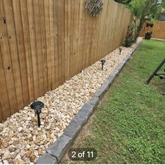 a backyard with rocks and gravel on the ground next to a wooden fence that has a black bird feeder in it