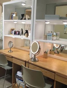 a desk with two chairs and a mirror on it in front of some shelves filled with personal items