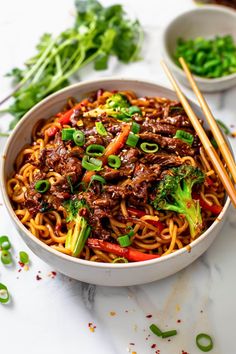 a bowl filled with beef and noodles next to chopsticks