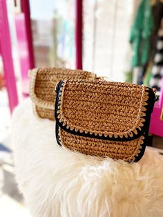 two straw purses sitting on top of a white furnishing cushion in front of a store window