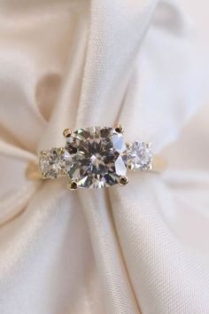 an engagement ring with three stones on it sitting on top of a white satin fabric