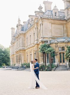 a bride and groom standing in front of a large building with trees on the other side