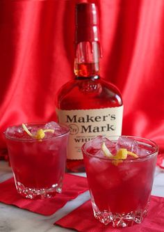 a bottle of maker's mark and two glasses filled with red liquid on a table