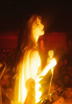 a woman standing in front of a crowd holding a small object with her right hand