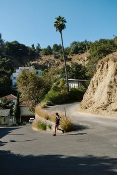 a person is walking down the street in front of a hill and palm tree on a sunny day